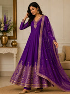 Woman wearing a purple traditional outfit with gold embroidery in a decorated room.