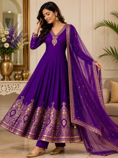Woman wearing a purple traditional outfit with intricate designs in a decorated room.